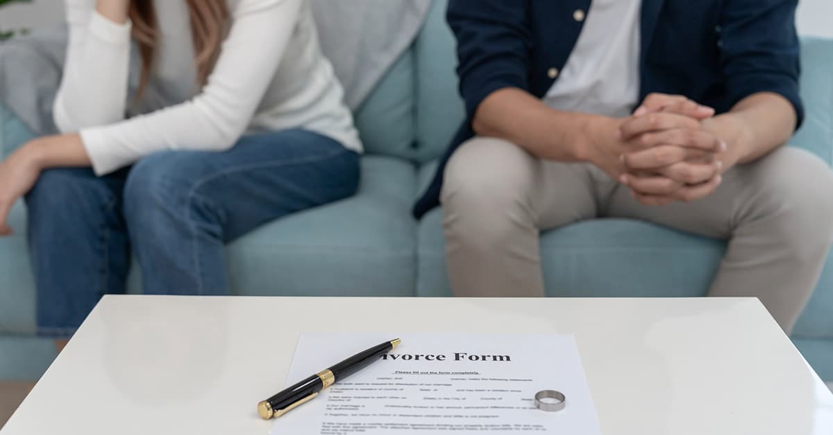 Couple sitting apart with divorce paperwork and wedding ring on table